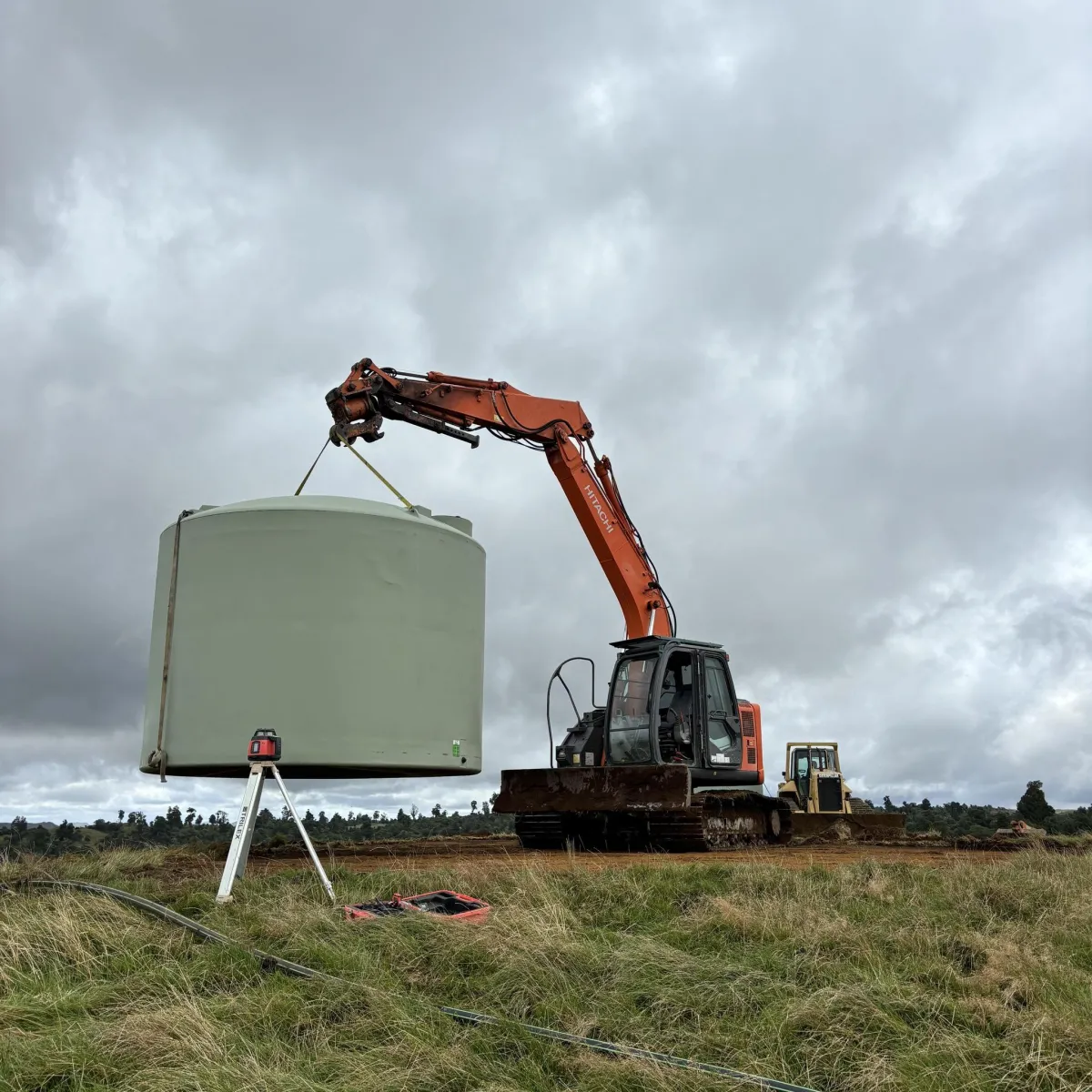 Excavator placing a large concrete tank for farm infrastructure at a building site.