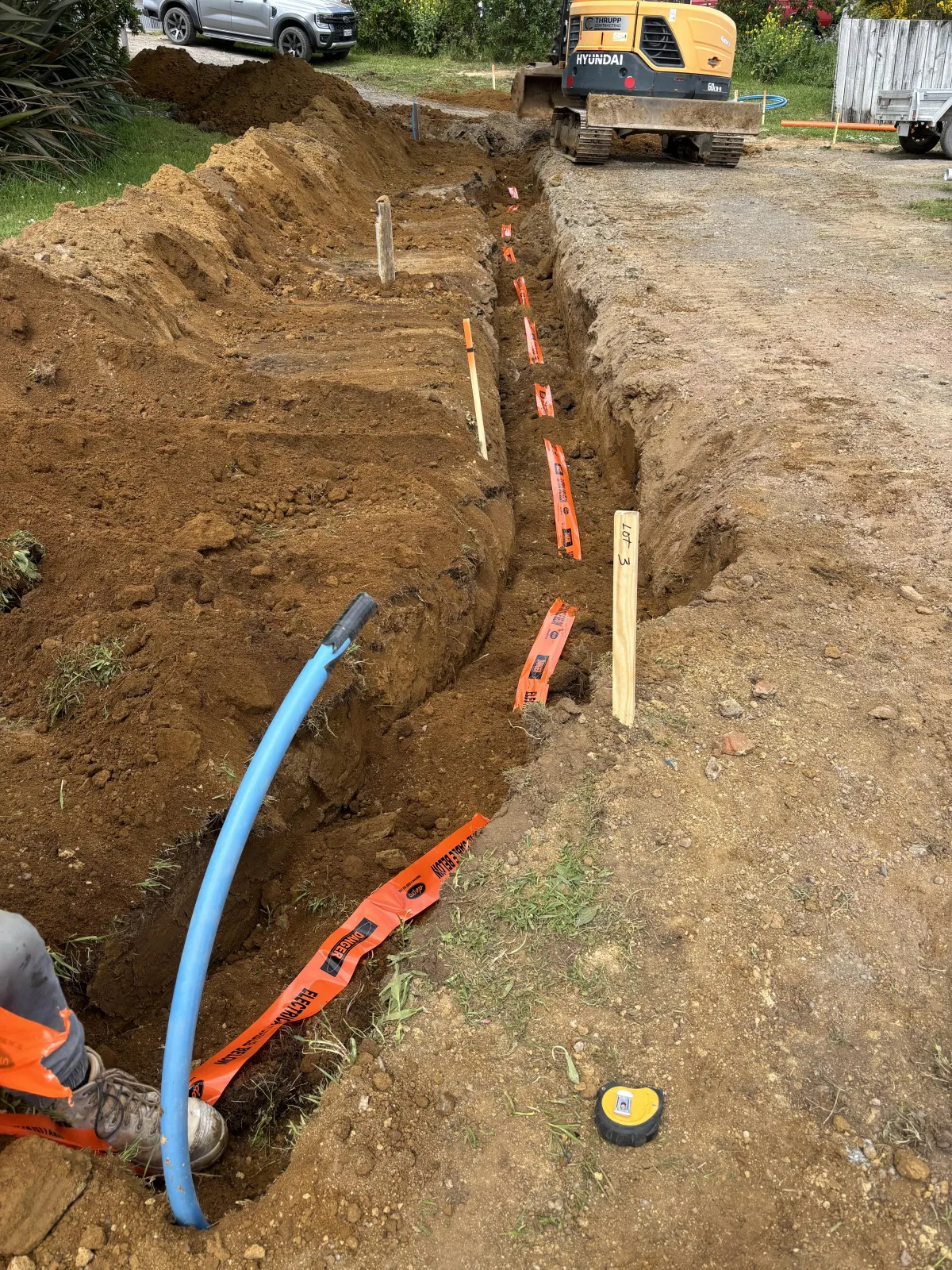 Underground services installation with worker digging trench and laying pipes in Ohakune.