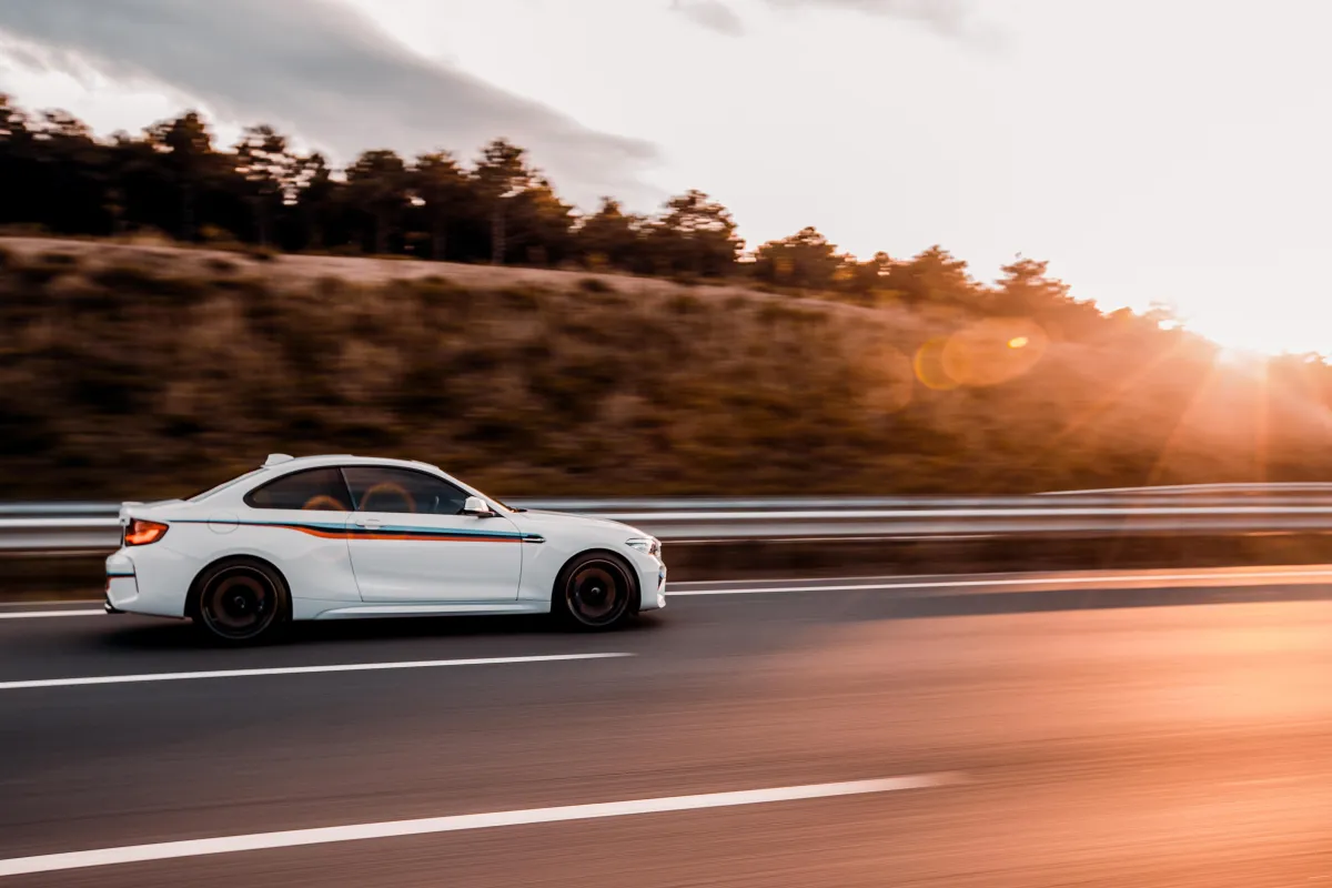 White car driving on the road at sunset, representing why running ads a dealership is important for sales growth.
