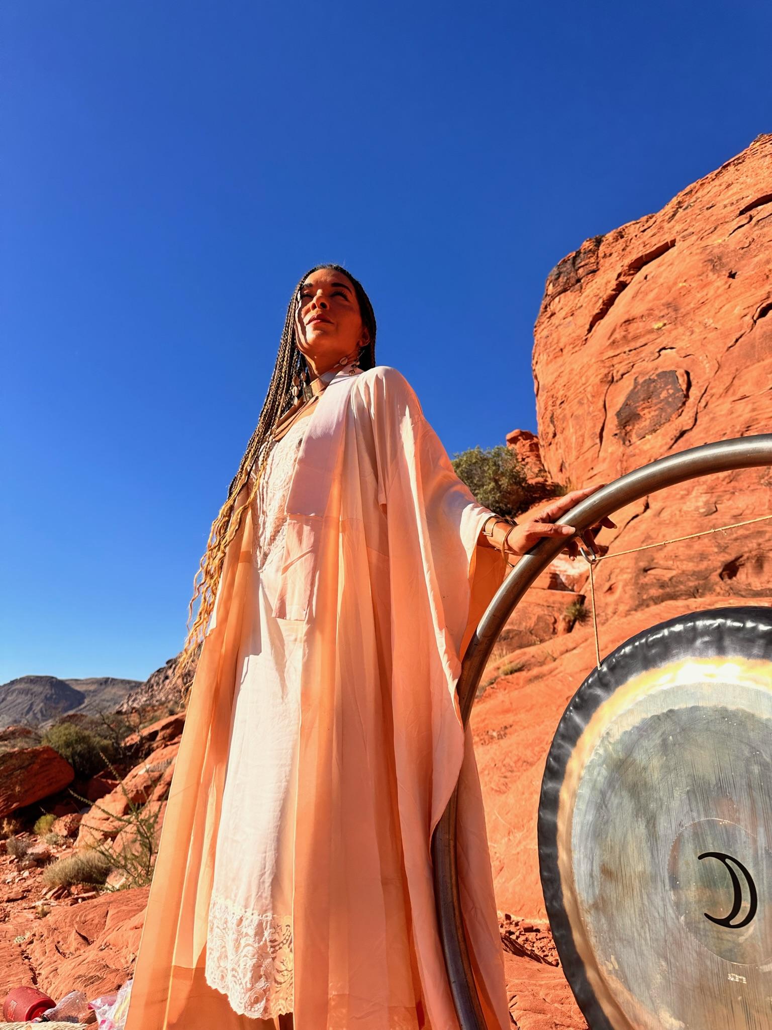 Woman in a colorful flowing dress standing inside a large A-frame wooden structure outdoors.