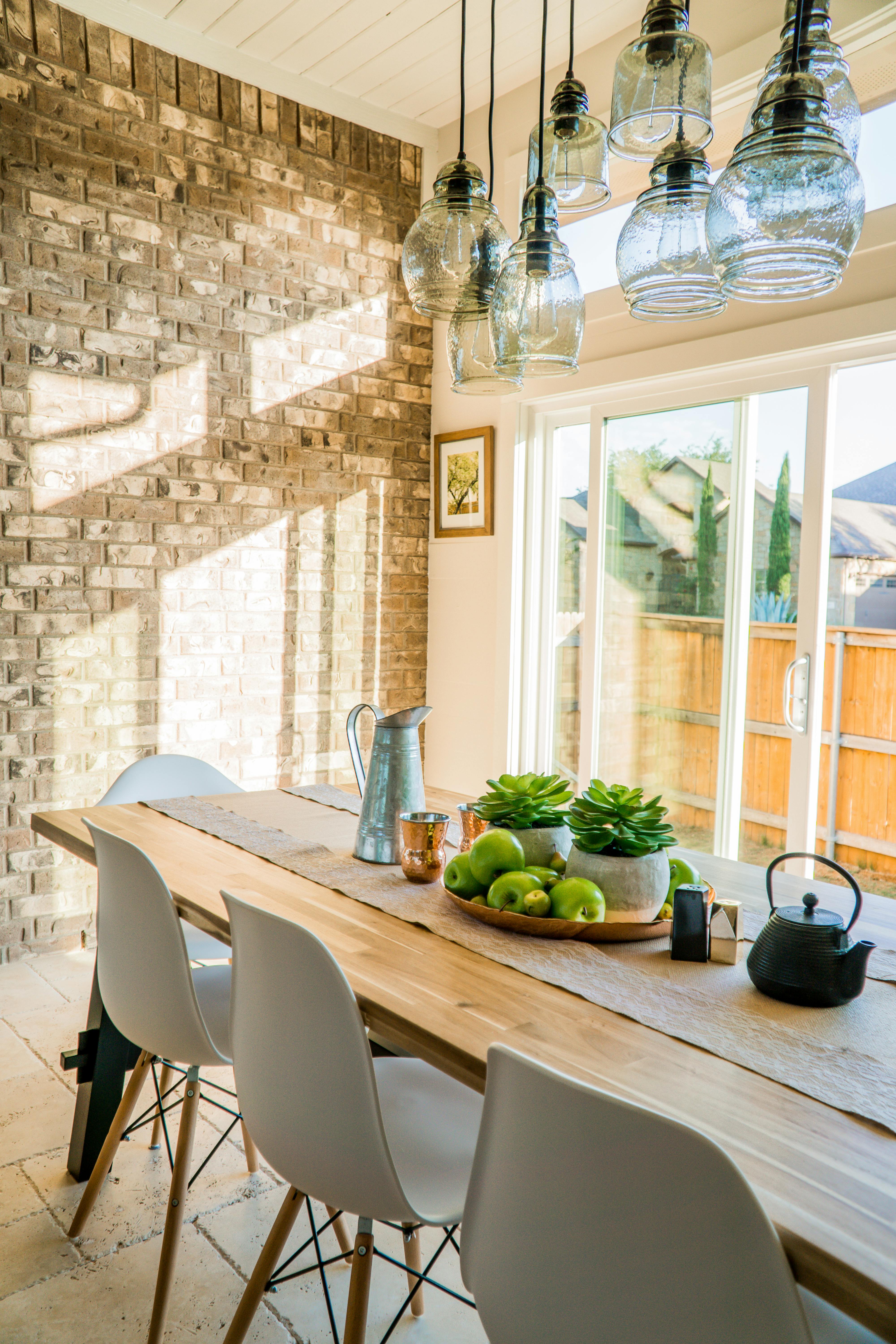 Stylish dining area with wooden table, modern chairs, hanging glass lights, and sunlight creating a warm, inviting interior