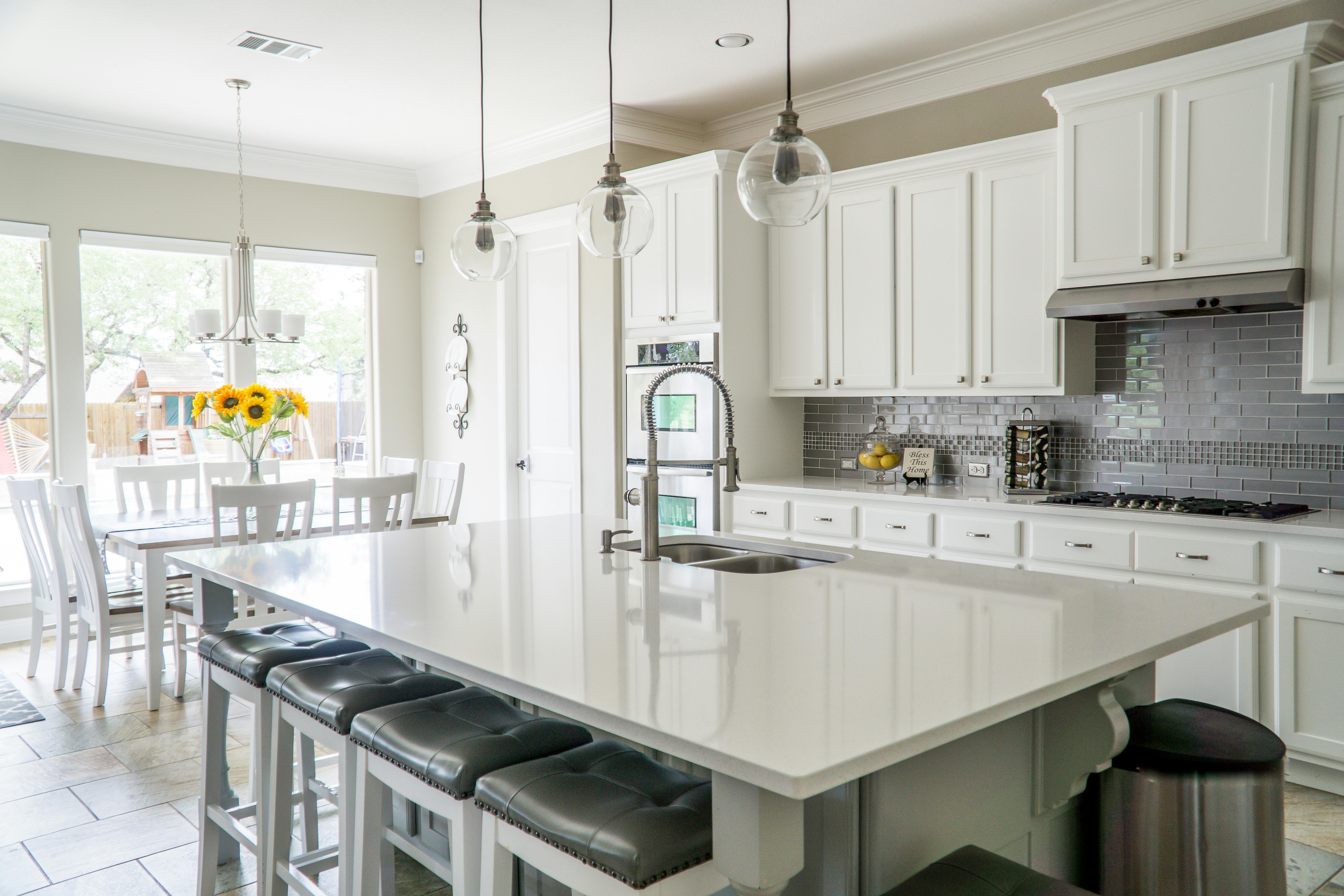 Modern white kitchen with large island, bar stools, pendant lighting, and bright natural light creating a clean, elegant space