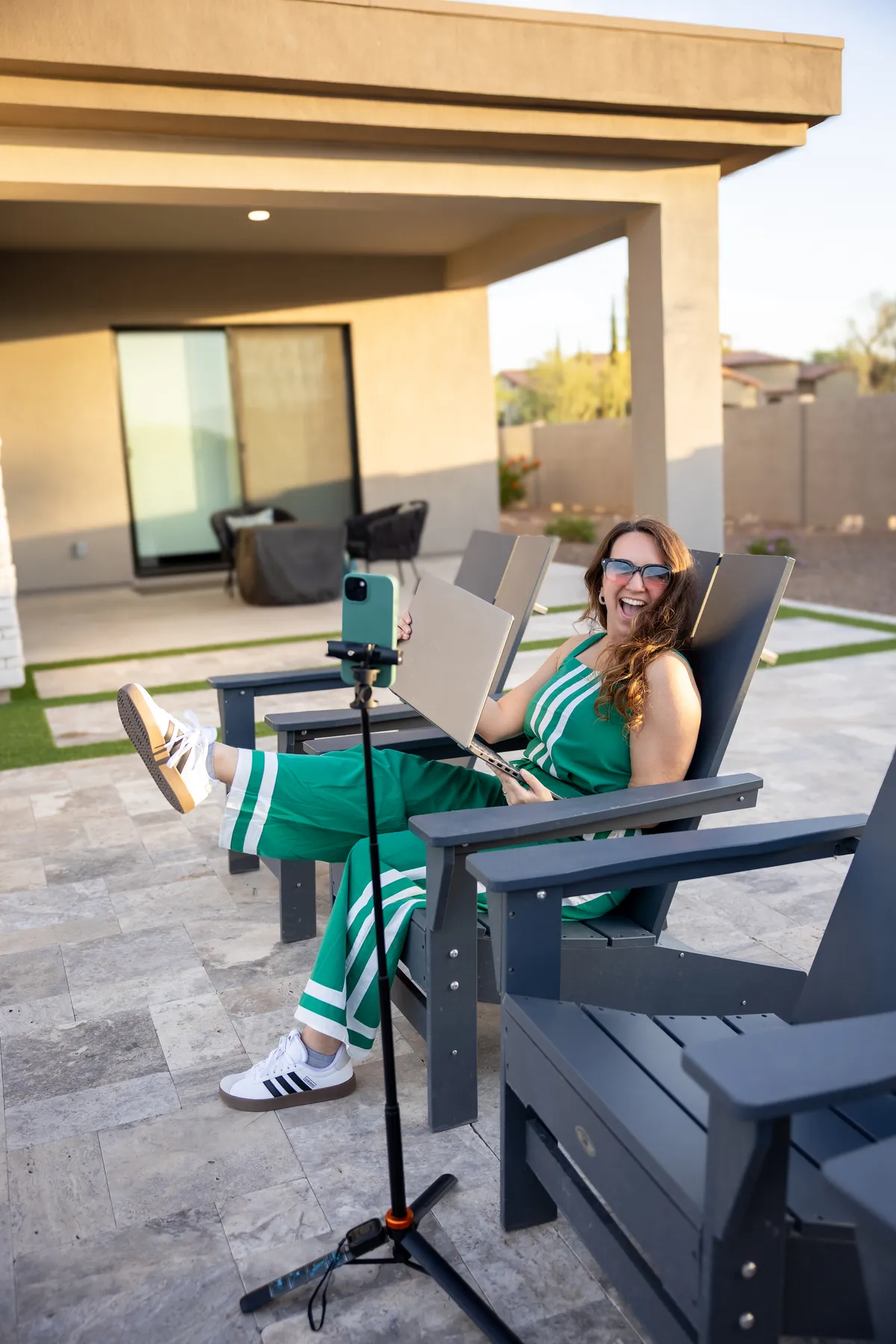 Woman sitting sideways on a modern blue velvet sofa, smiling, filming herself with a smartphone on a tripod.