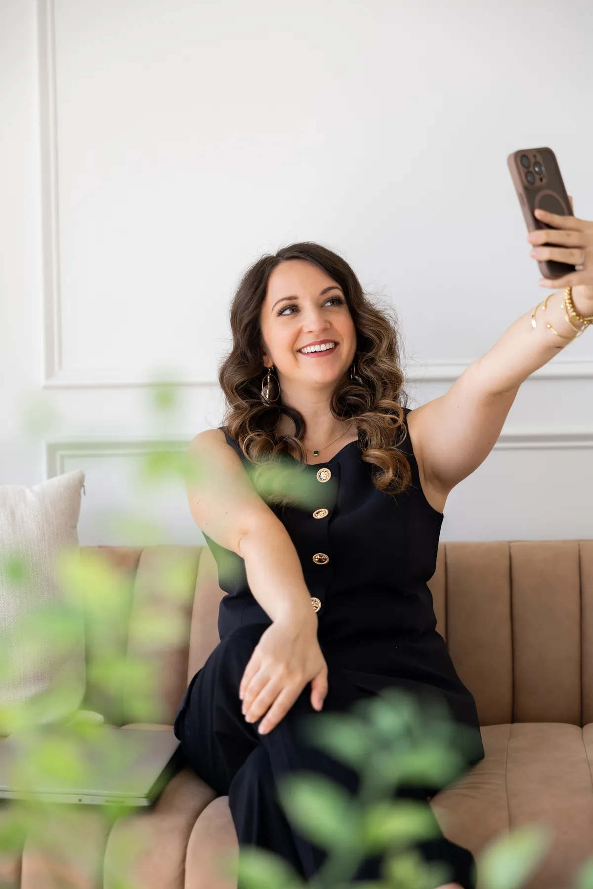 Woman sitting casually on a white kitchen counter holding a laptop, wearing jeans and white boots, bright airy lighting