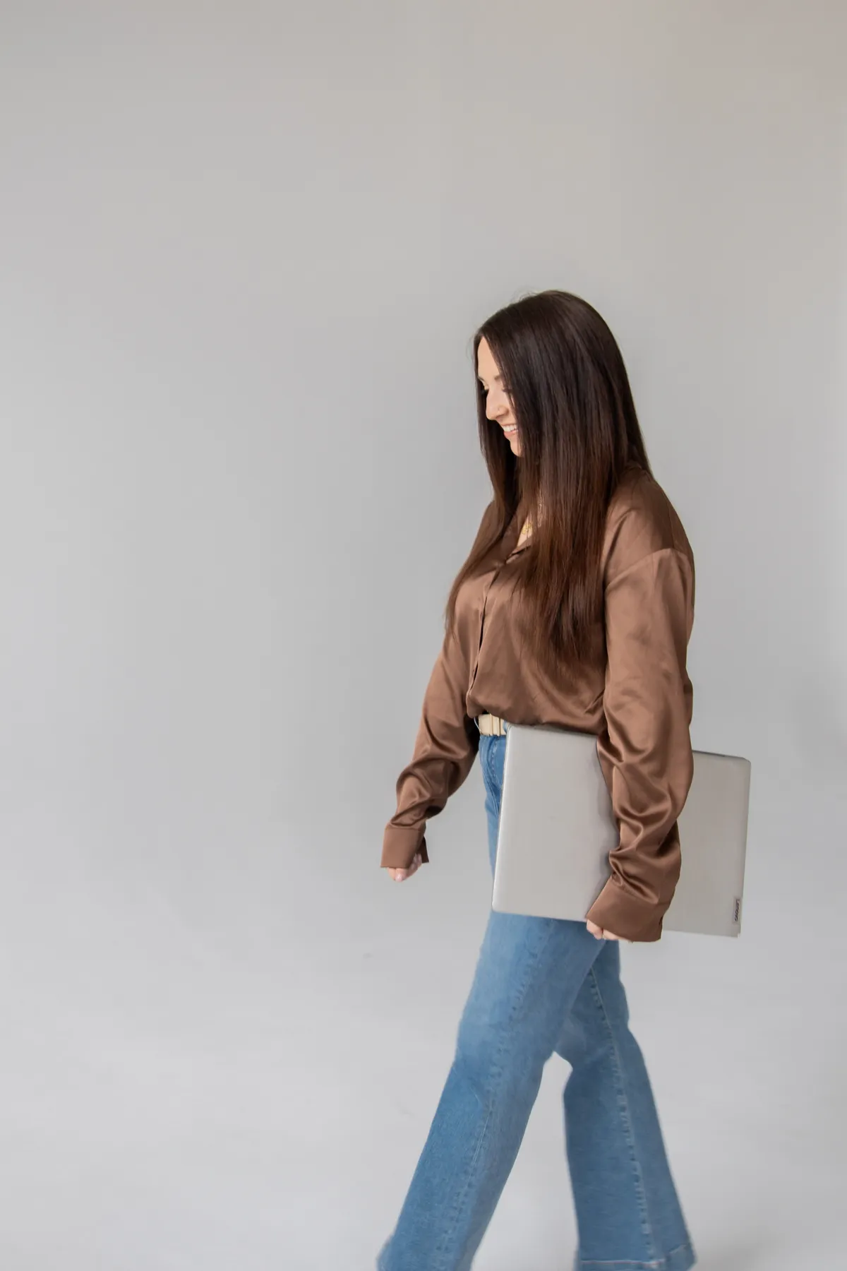 Woman standing against a seamless light grey backdrop, holding a camera and wearing casual clothes.