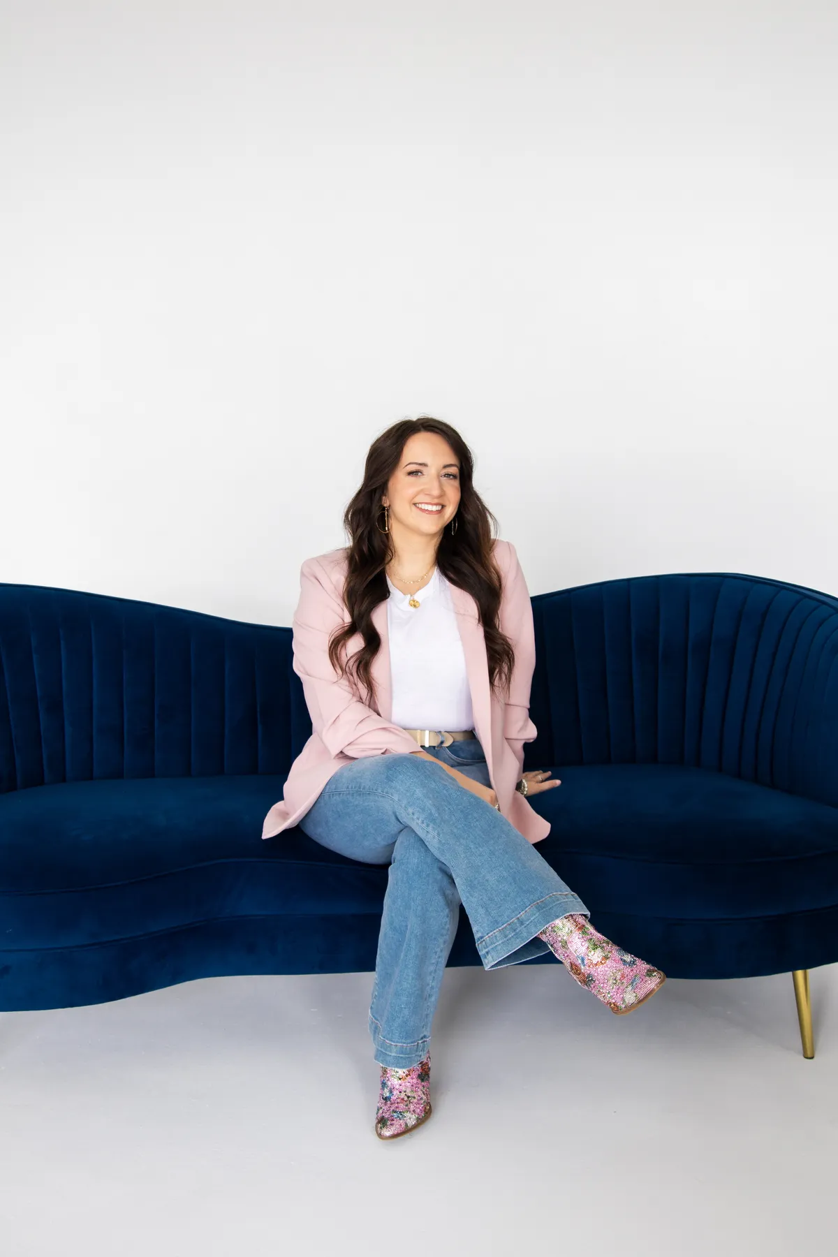 Woman with long dark hair smiling and working on a laptop while sitting in a green velvet chair.