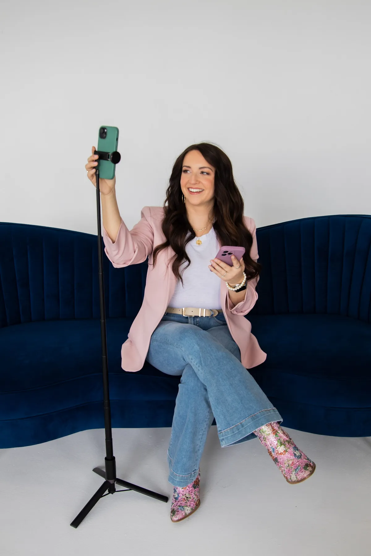 Woman seated in a black chair taking a selfie with her phone, modern bright setting with a small plant on a stool