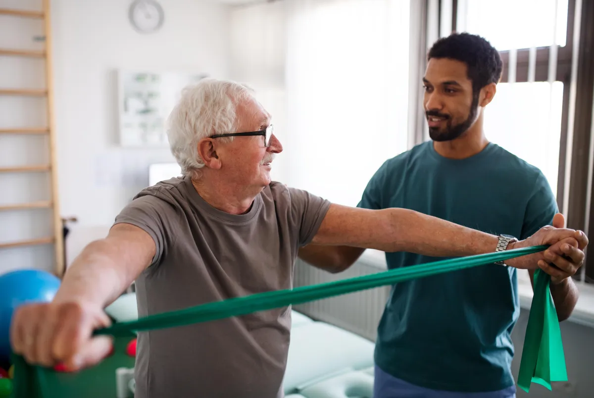 therapist doing shoulder strengthening exercises with elderly male patient