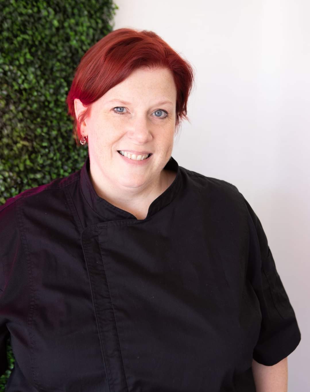 Pastry Chef Erica Bentson in a black chef coat against a green hedge backdrop