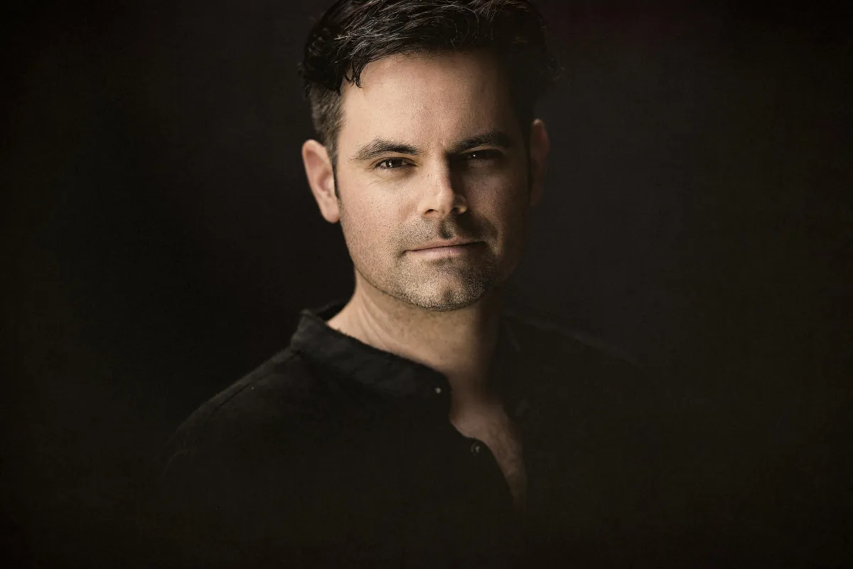 Max Trombly - Man with dark hair and a trimmed beard, in a dark shirt