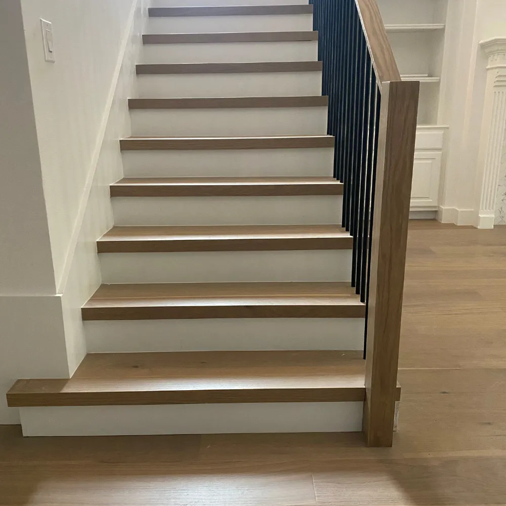 Modern staircase with wood treads, white risers, and a sleek black metal railing, leading to a well-lit interior space.