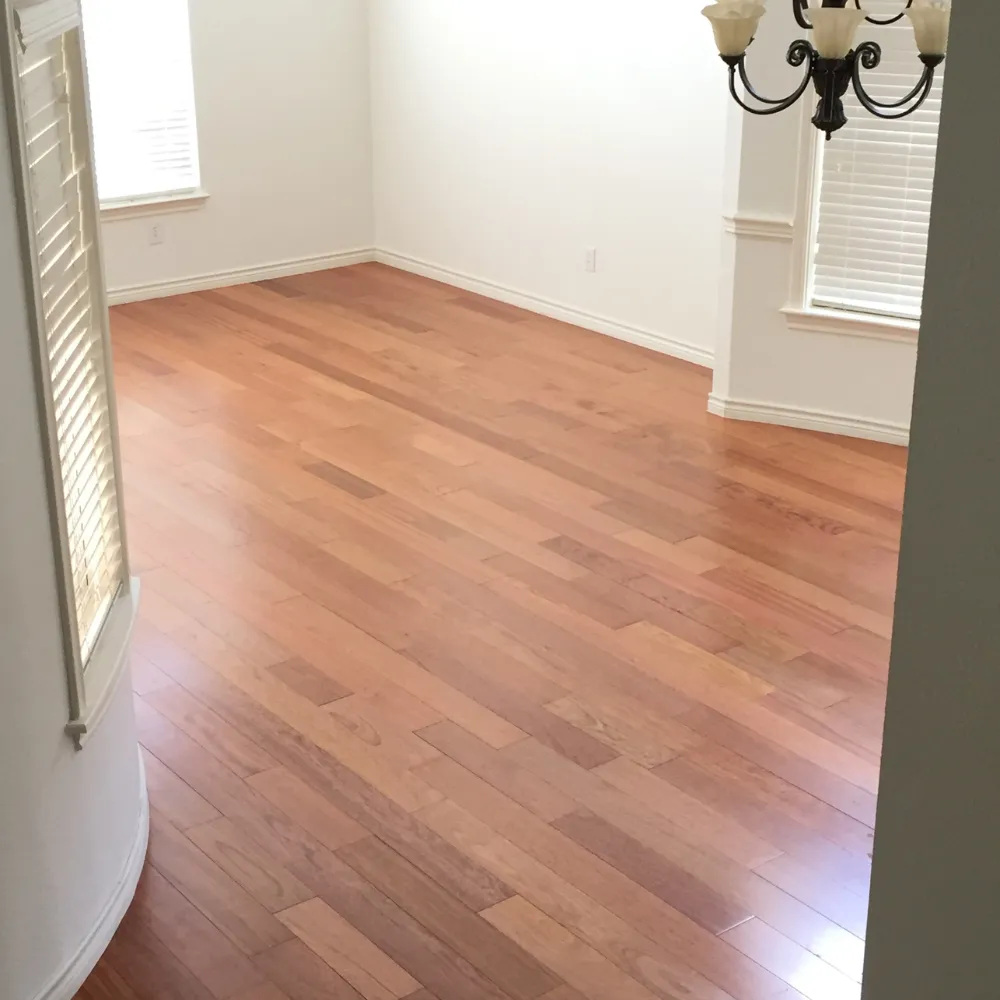 Bright dining area with warm cherry wood flooring, white walls, crown molding, and natural light streaming through multiple windows, complemented by a classic chandelier.