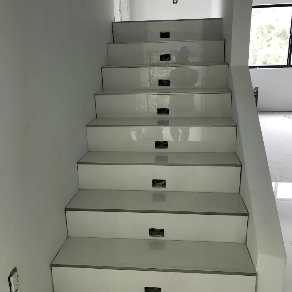 Modern staircase with glossy white steps, inset lighting placements, and sleek minimalistic design, leading to a bright, open space with a large window.