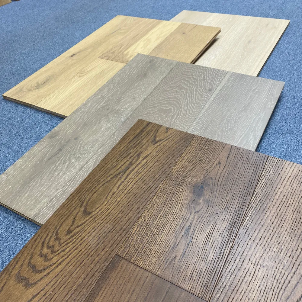  Selection of wooden flooring samples in various finishes, including light oak, gray, and rich walnut, displayed on a gray carpet background.