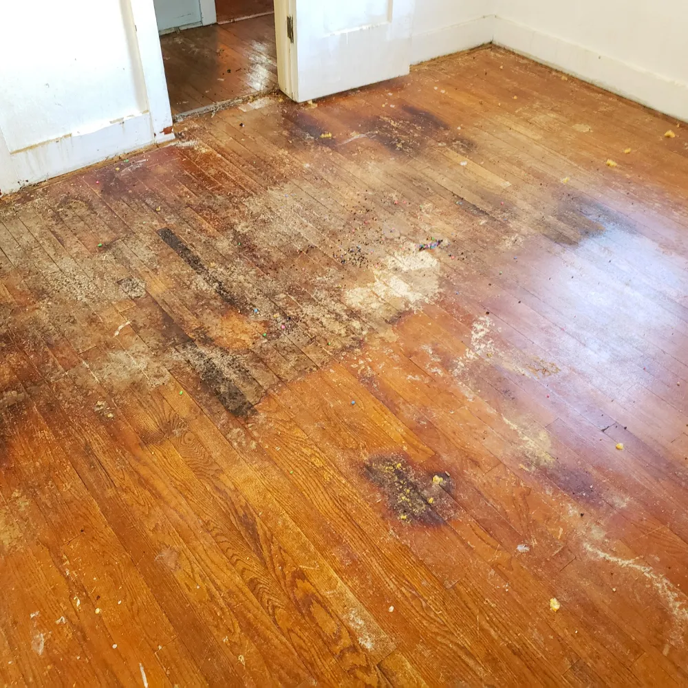 Damaged hardwood flooring with extensive stains, discoloration, and wear, showing the need for refinishing or replacement.