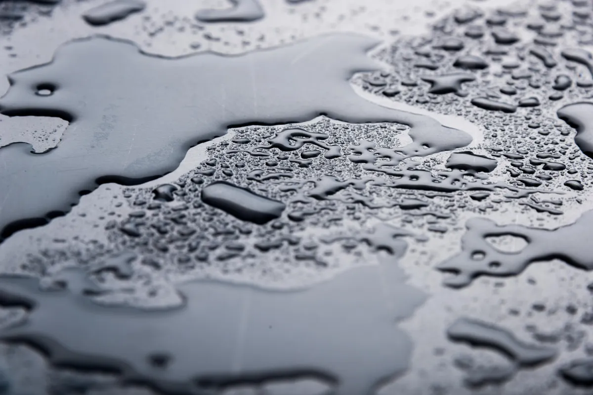 Close-up view of water droplets and small puddles on a dark, smooth surface, highlighting moisture accumulation and potential water damage risk.