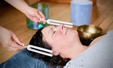 Sound healing practitioner using tuning forks around a client’s head during a vibrational therapy session.