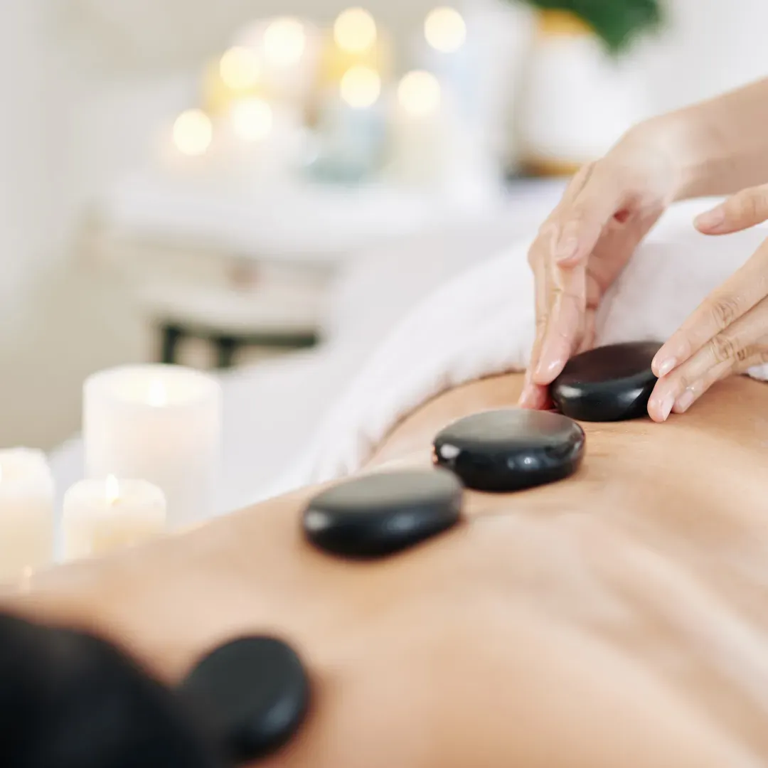 Warm basalt stones placed along a client’s back during a hot stone massage with candlelight in the background.