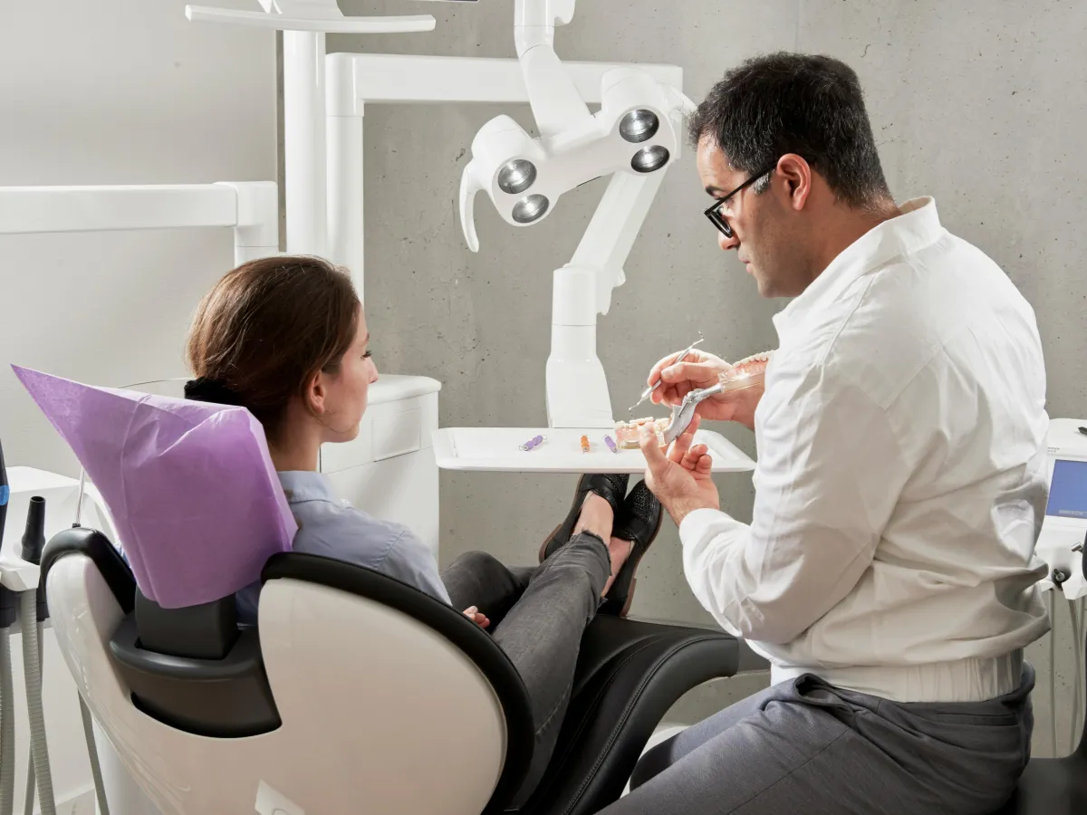 Dentist sitting in chair with dental model explaining something to patient in exam chair.