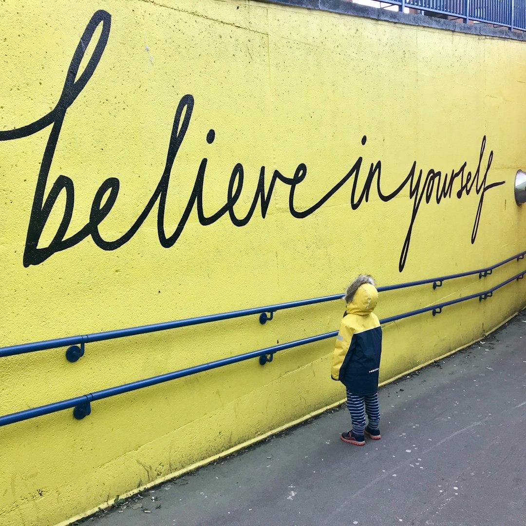 Yung child looking at yellow wall with the words Believe in yourself