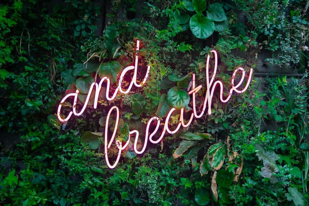 Green plant wall with neon sign with words and breathe