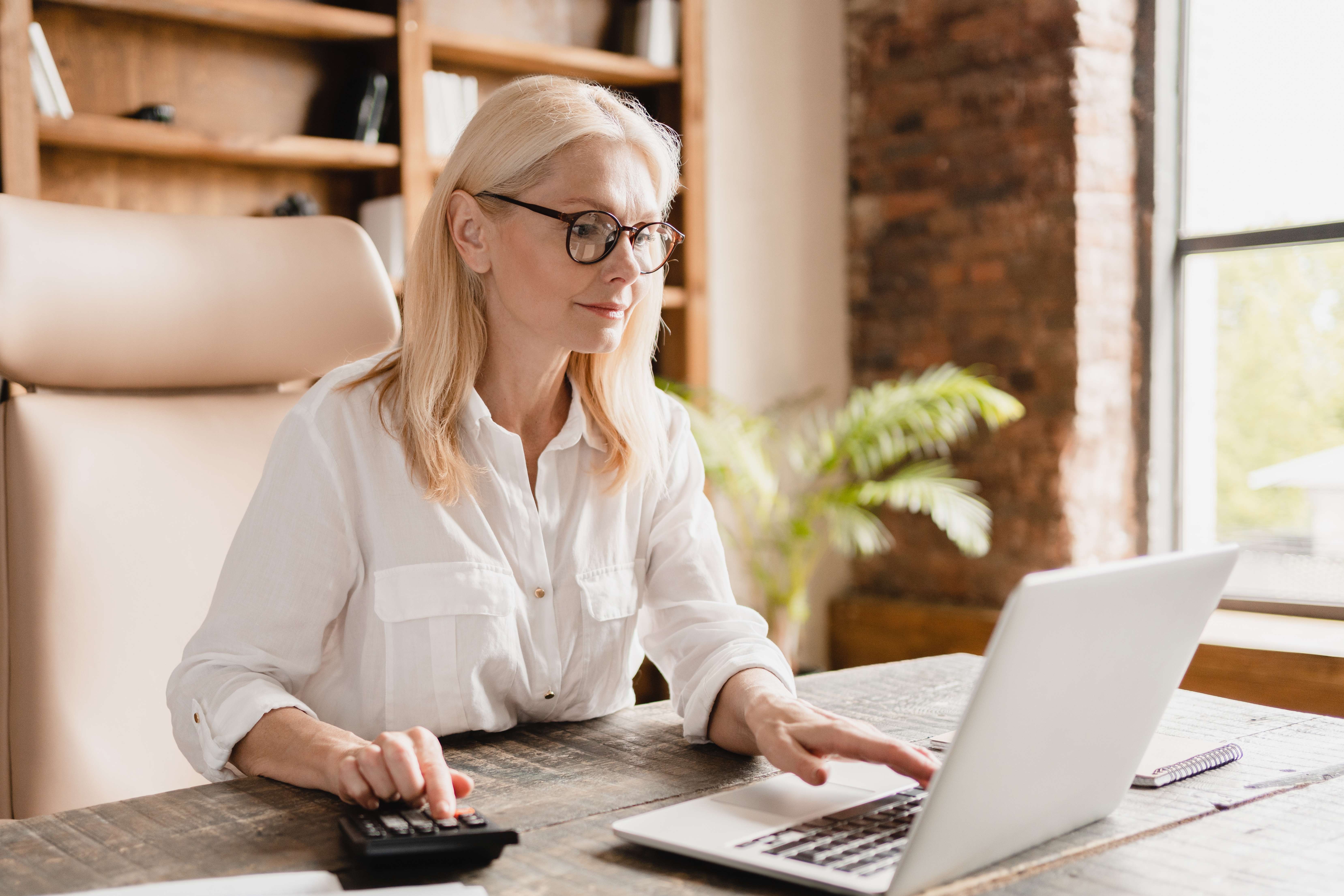 Woman in desk, typing on calculator in natural light.