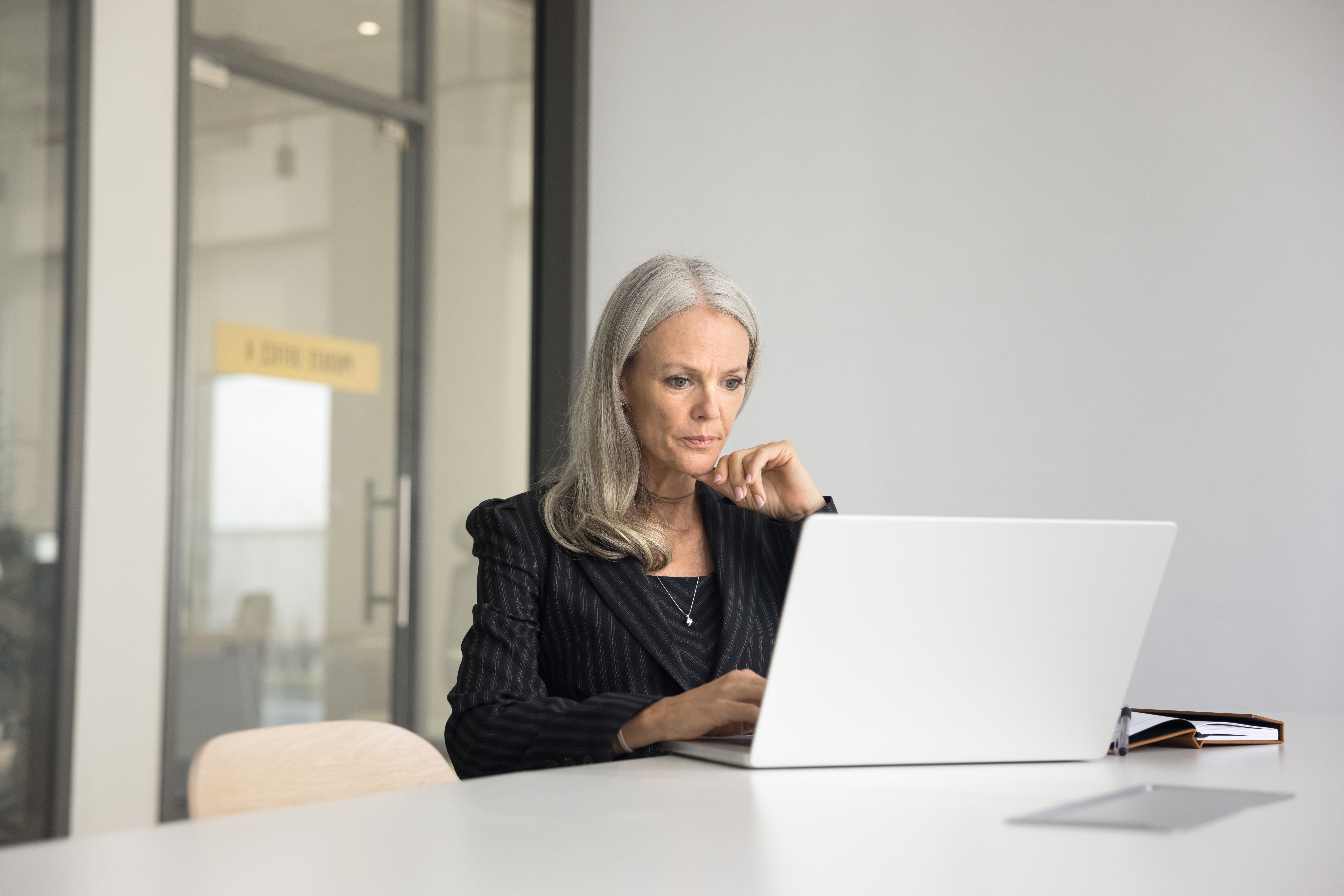 Mature professional woman on laptop in modern conference room.