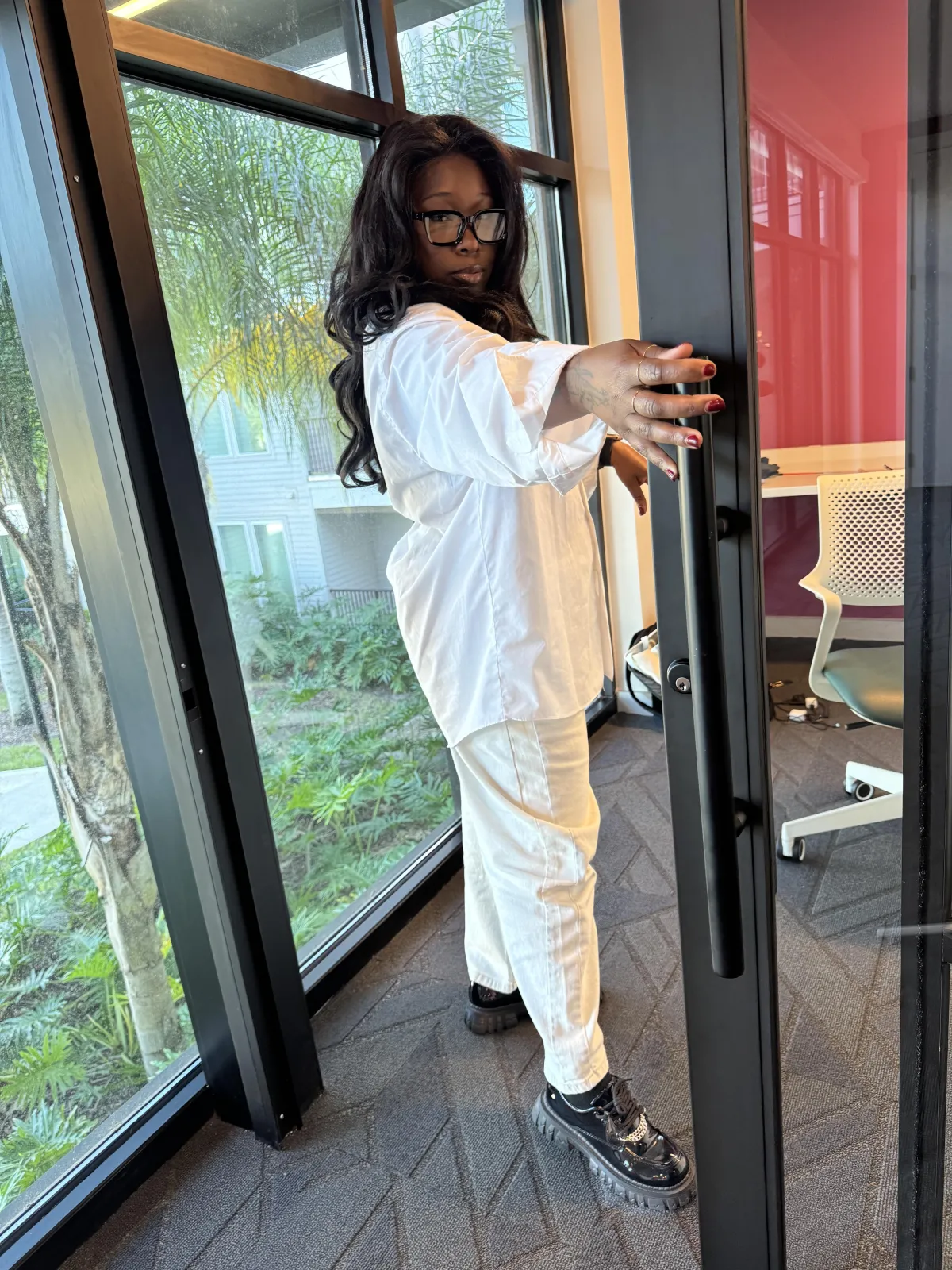 Danee, a 37-year-old woman with warm brown skin and shoulder-length curls, wearing a tailored cream blazer and subtle cross necklace, smiling confidently at camera, hands folded, studio-quality, photorealistic, shadow-free isolated portrait.