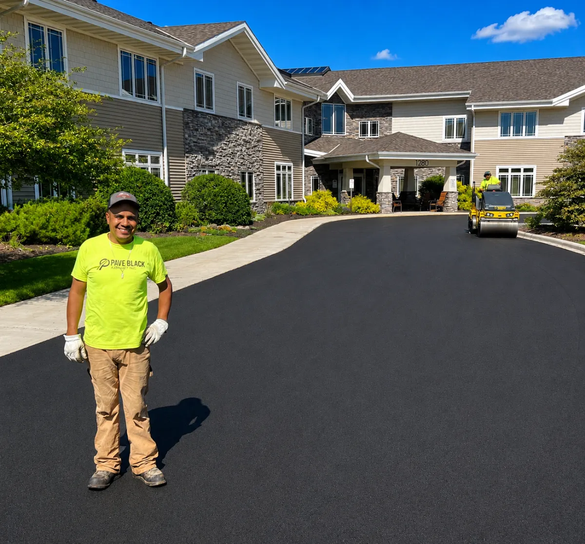 Pave Black Asphalt crew member standing on a newly paved commercial driveway in Appleton, Wisconsin, with an asphalt roller in the background