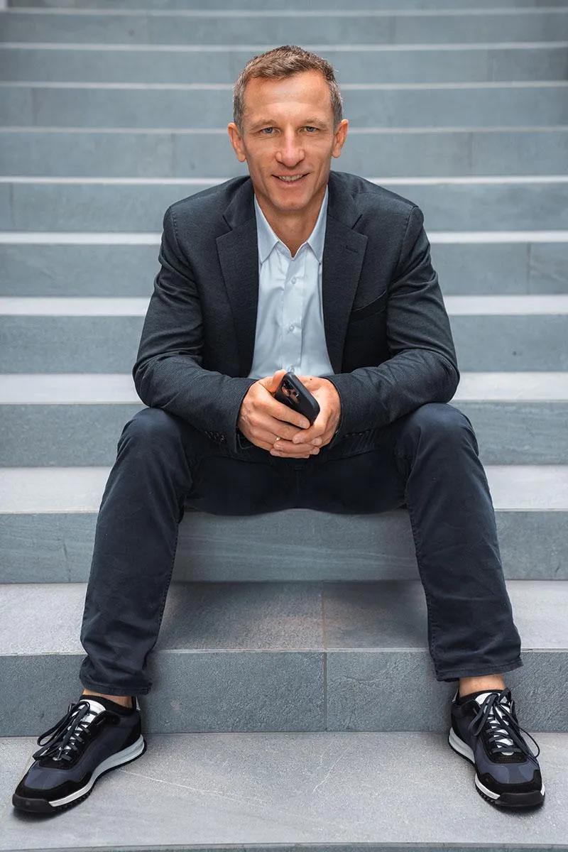 Falko Krismayr, network marketing expert, smiling confidently on stage, wearing a casual blazer and engaging with the audience.
