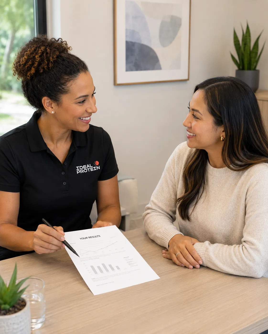A certified Ideal Protein coach in a branded uniform reviewing a results sheet with a client, showing the dedicated one-on-one support of the Ideal Protein GLP-1 Partner Program