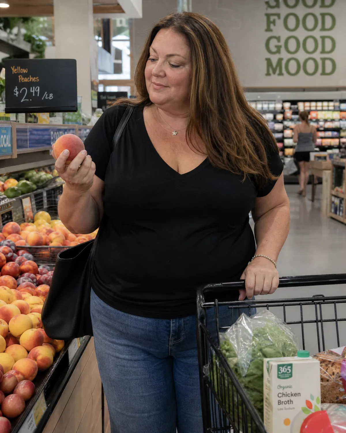 Woman shopping for fresh produce in a grocery store, selecting fruit while pushing a cart with vegetables and whole foods, representing healthy eating on a medically guided weight loss program