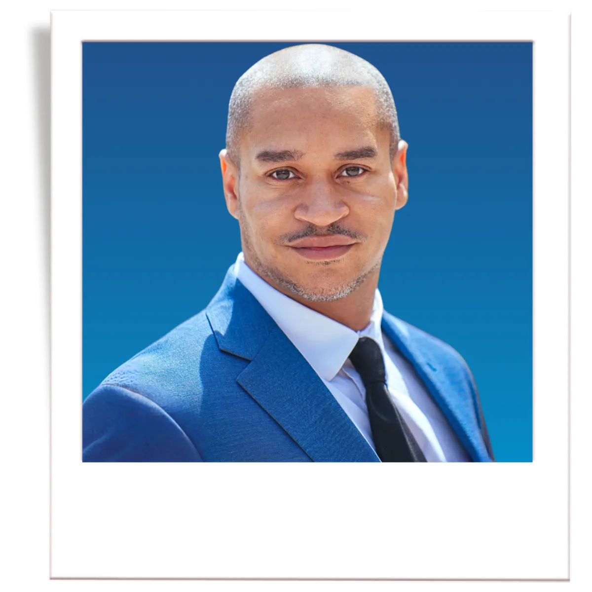 A picture of professional insurance agent, Noe Recendez. The picture is in the style of a polaroid. The insurance agent is wearing a dark grey men's blazer, a blue button down shirt, and a black tie. The agent is in front of a blue gradient background. 