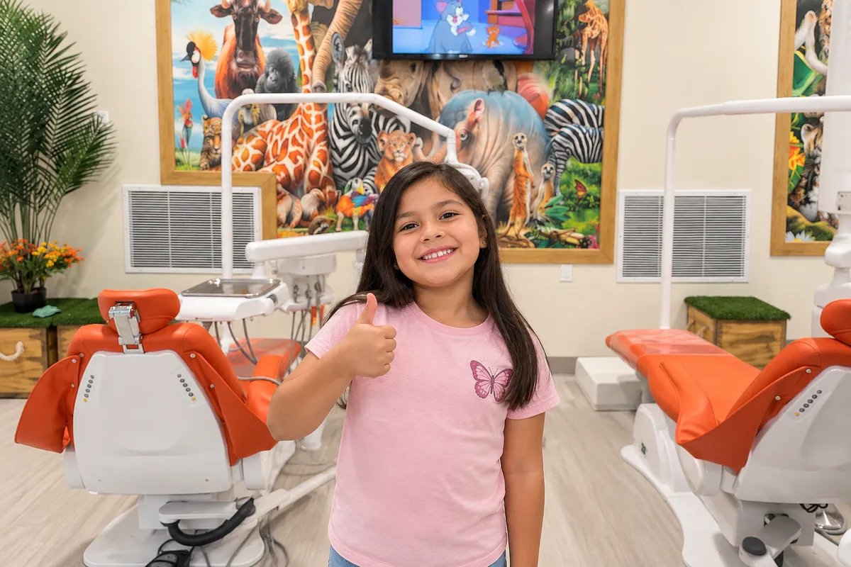 Smiling young girl giving a thumbs-up inside Amazon Children Dental's colorful pediatric dental clinic.
