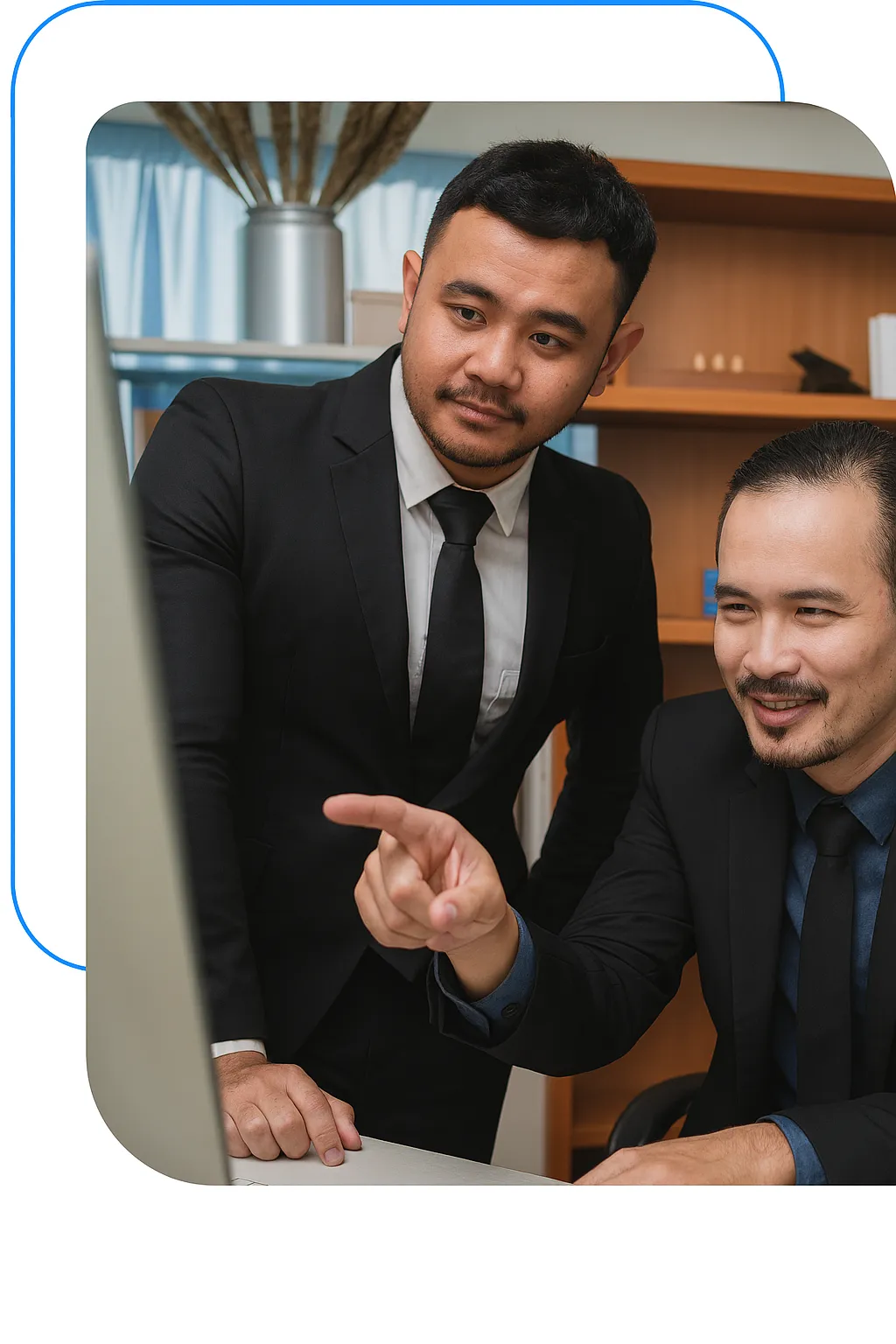 Two men in business suits collaborating at a desk, one pointing at a computer screen, reflecting teamwork and professional engagement in a modern office setting.