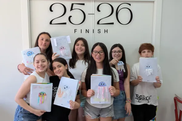 Un gruppo di sette giovani studenti sorridenti si trova di fronte a una porta bianca, mettendo in mostra le loro creazioni artistiche su fogli di carta. Ognuno tiene in mano un disegno unico di una medusa, mostrando dettagli colorati e creatività. I disegni mostrano diverse interpretazioni stilistiche della medusa. Sopra le teste degli studenti, sulla porta bianca, è visibile la scritta "25-26 FINISH", indicando il completamento di un progetto o anno scolastico. L'atmosfera è allegra e piena di orgoglio per i loro lavori.