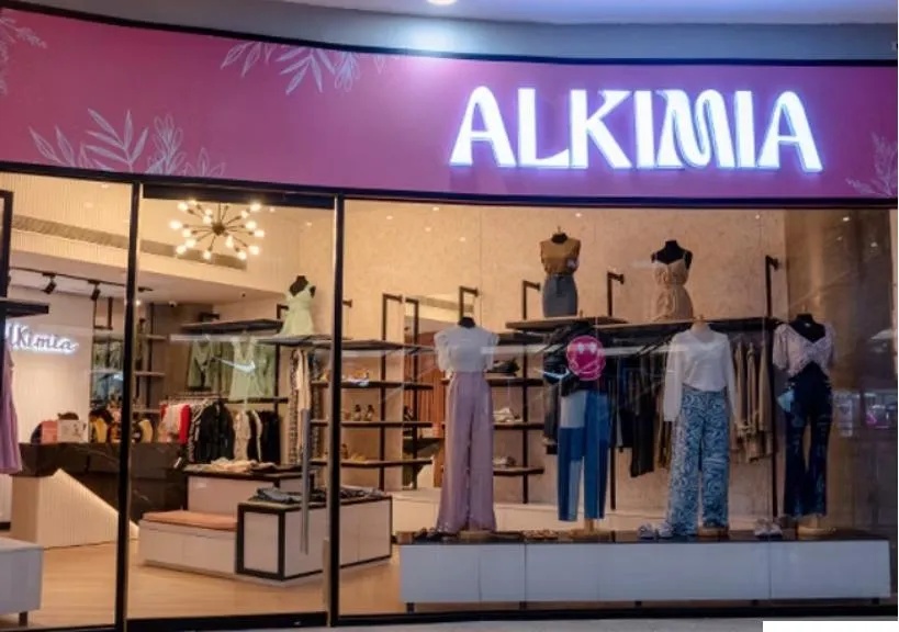 Mujer joven con vestido rosa pastel de Alkimia, fondo minimalista blanco, detalles de tela premium y accesorios dorados, expresión confiada y elegante, luz suave, composición vertical, estilo editorial