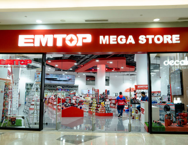 Primer plano de un profesional venezolano usando una llave de impacto EMTOP en un sitio de construcción moderno, con fondo desenfocado azul y rojo, mostrando concentración y precisión en la tarea.