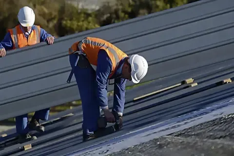 Two workers fastening metal roofing panels on commercial building in Blaine by Blaine Commercial Roofing