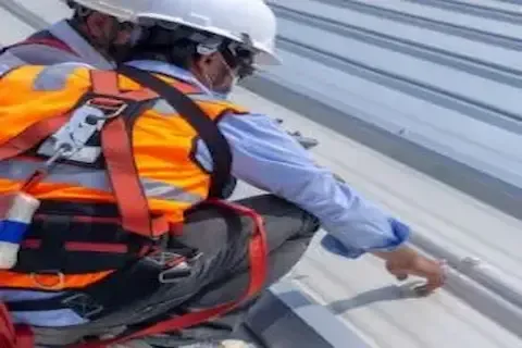 Roofing technician in safety harness inspecting metal roof seams for preventive maintenance