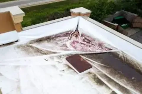 Torn and water-damaged flat roof membrane after storm on commercial property