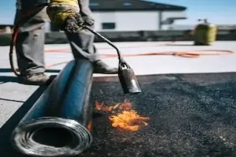 Blaine Commercial Roofing technician torch-applying modified bitumen sheet to commercial roof