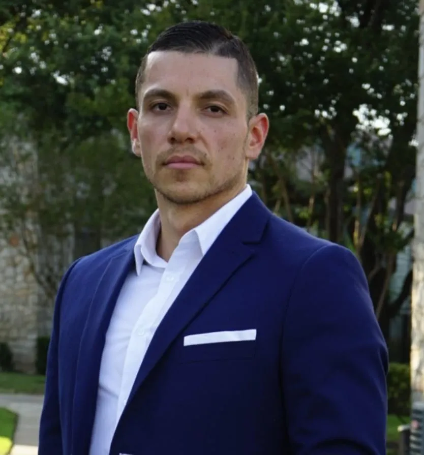 Brandon Garcia, founder of Full Circle Media, dressed in a blue suit and white shirt, standing outdoors with trees and a building in the background.