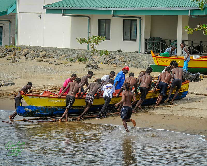 Villagers in Saint Lucia helping fishermen pull a colorful fishing canoe onto the beach after returning from a day at sea