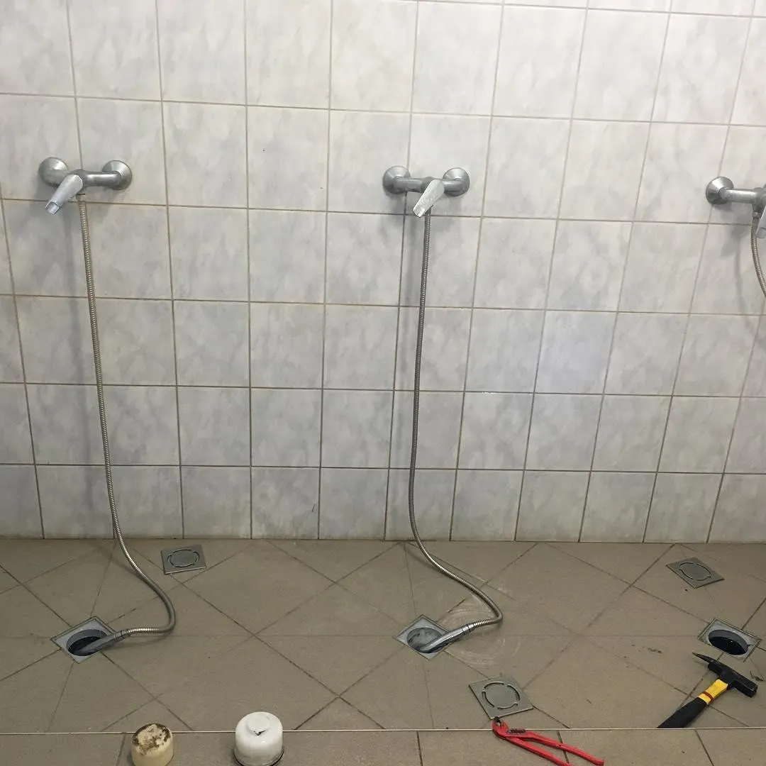 Three disconnected shower heads on a tiled wall; hoses lie on the floor. Tools like pliers and a wrench indicate ongoing repairs.