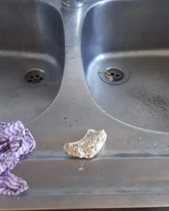 A metal double sink with a stained surface. A tattered purple cloth and a broken piece of concrete lie on the countertop, suggesting disarray.