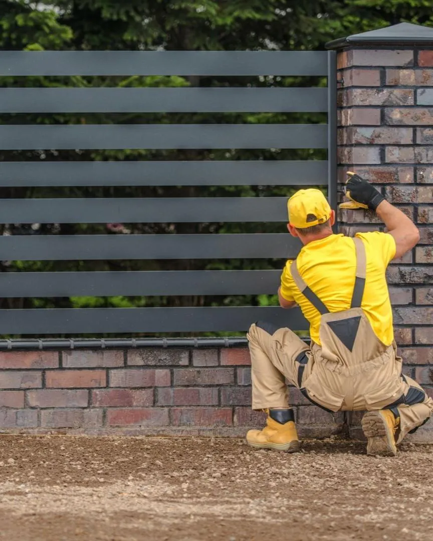 Professional installer building a modern metal fence with brick posts in Carrollton TX for residential property security and style.