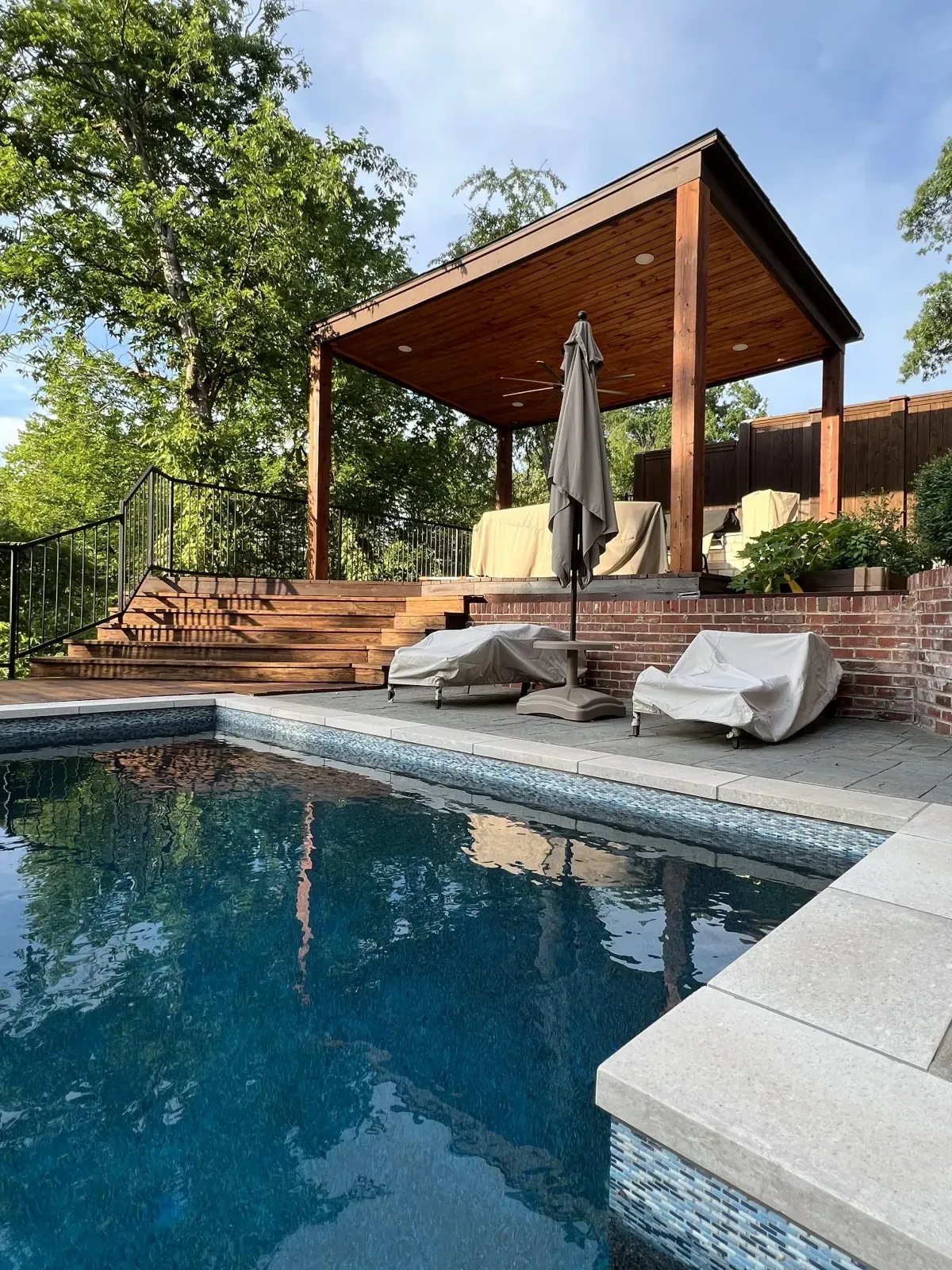 Modern covered pergola built next to a pool in Carrollton, TX, featuring wood posts, solid roof, and elevated deck for outdoor entertaining.