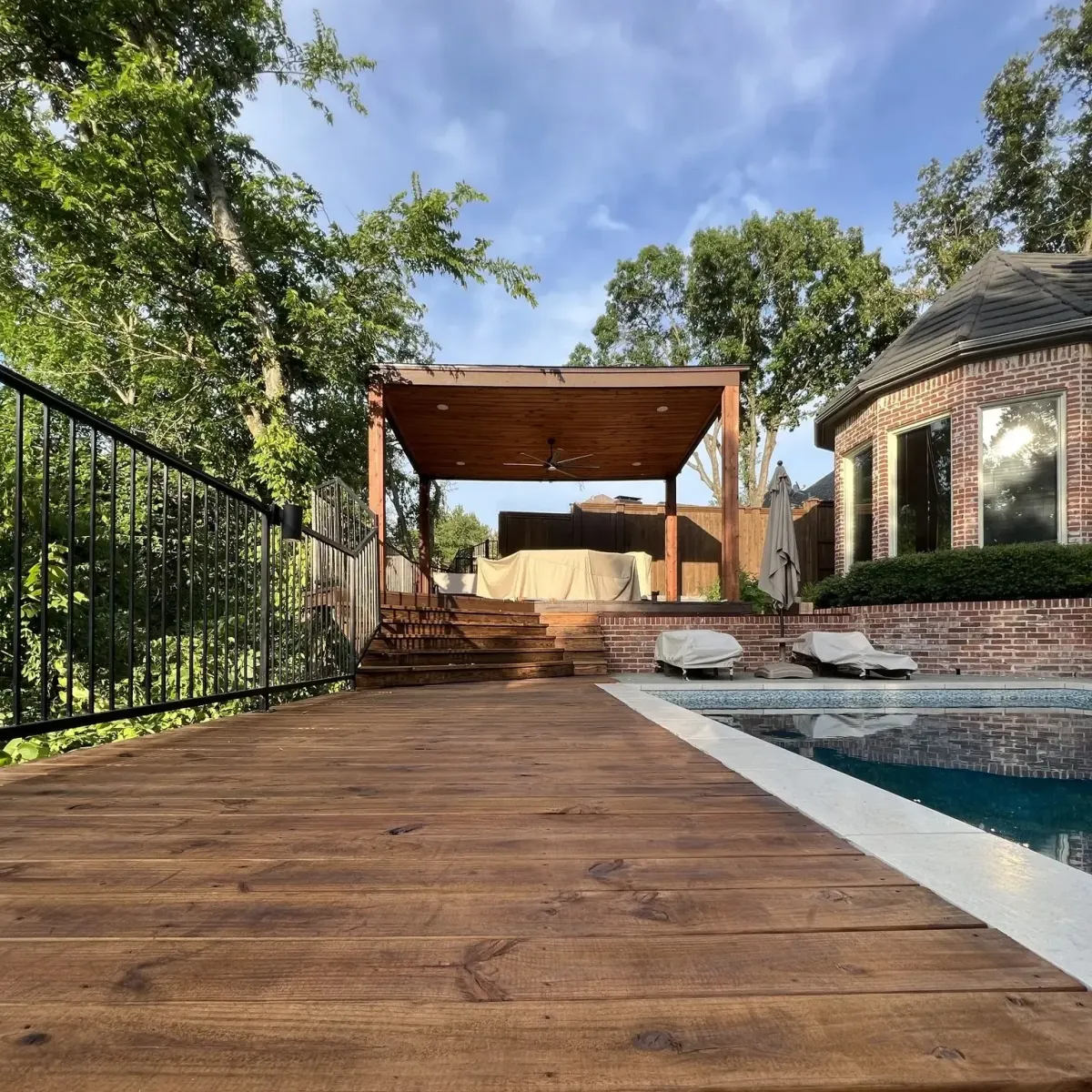 Custom covered pergola with flat roof and wood posts built beside a pool in a Carrollton, TX backyard, designed for shade and outdoor lounging.