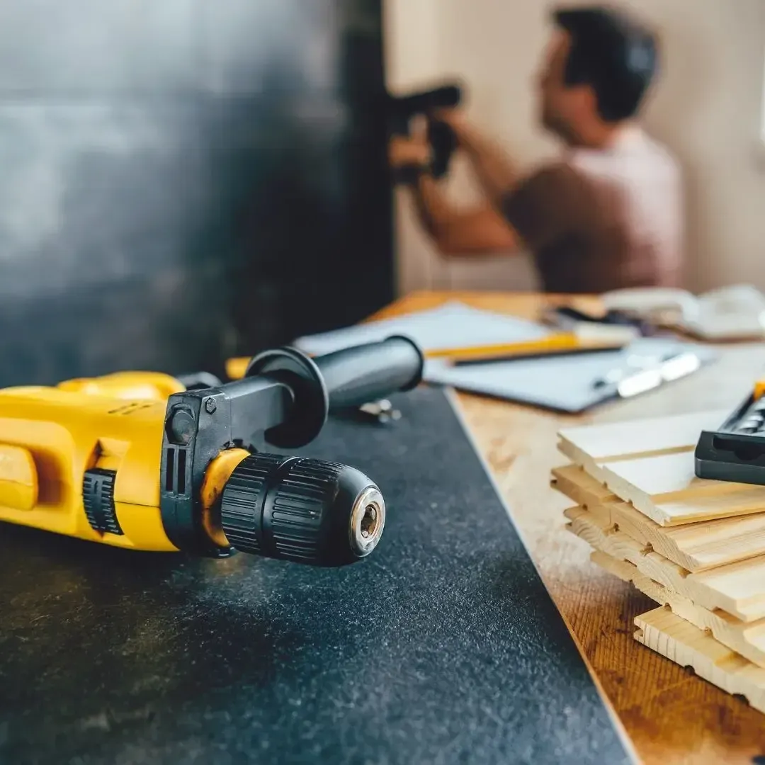 Close-up of drill, screws, and lumber on a workbench with a contractor working in the background during a Rowlett TX remodel by Texas Woodpeckers.